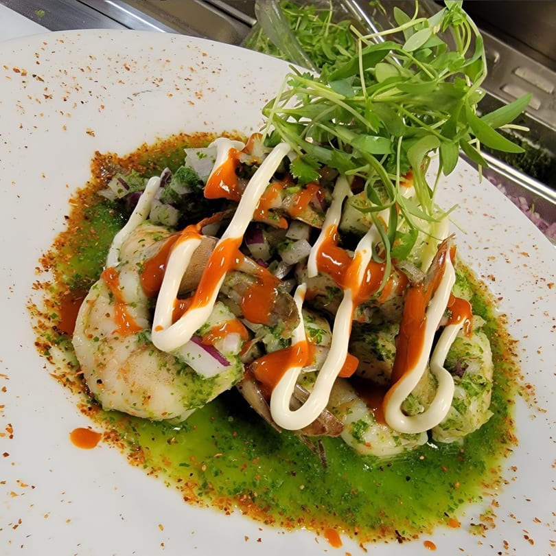 Shrimp ceviche with green sauce, red hot sauce, and white crema, garnished with fresh greens.