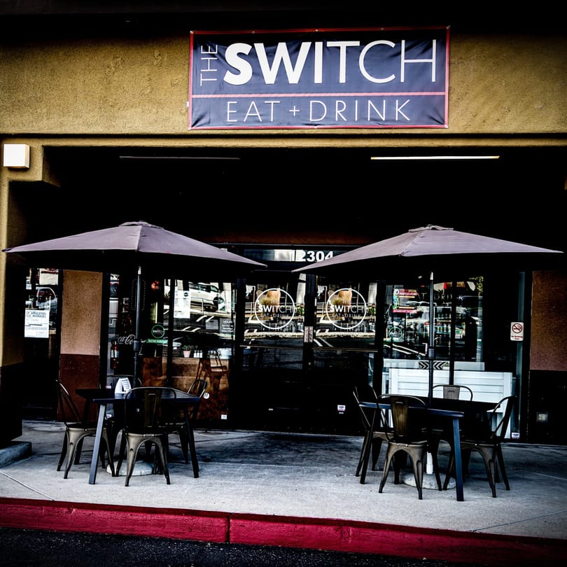 The Switch SLO restaurant exterior with outdoor seating, umbrellas, and a prominent "Eat + Drink" sign.
