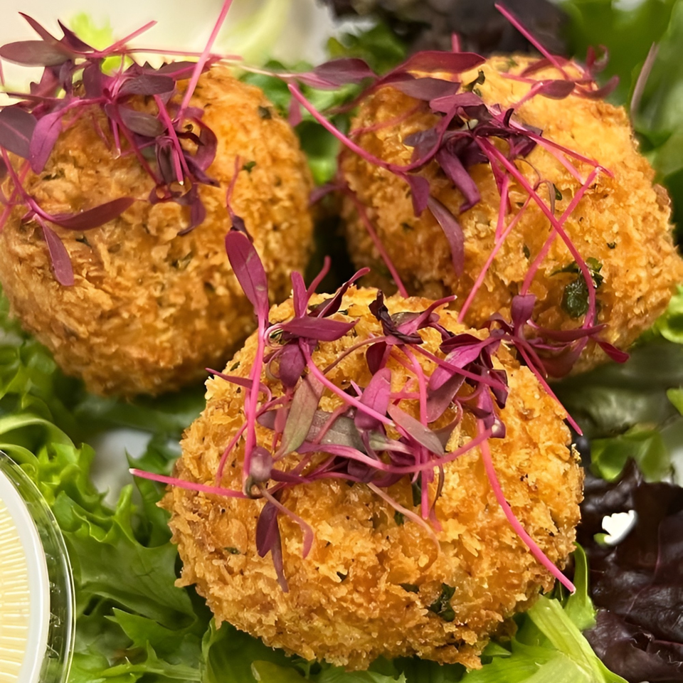 Three golden-brown fried balls, garnished with red microgreens, resting on a bed of fresh green lettuce.