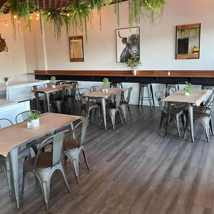 The Switch SLO dining room with metal tables and chairs, a long bar, and hanging plants.