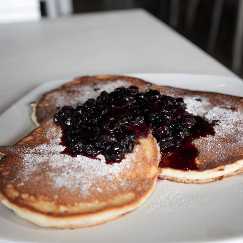 Fluffy pancakes topped with blueberry compote and powdered sugar on a white plate at The Switch SLO.
