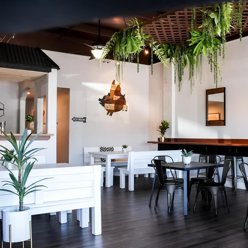 The Switch SLO dining room with white benches, black tables, hanging plants, and a pig decor.