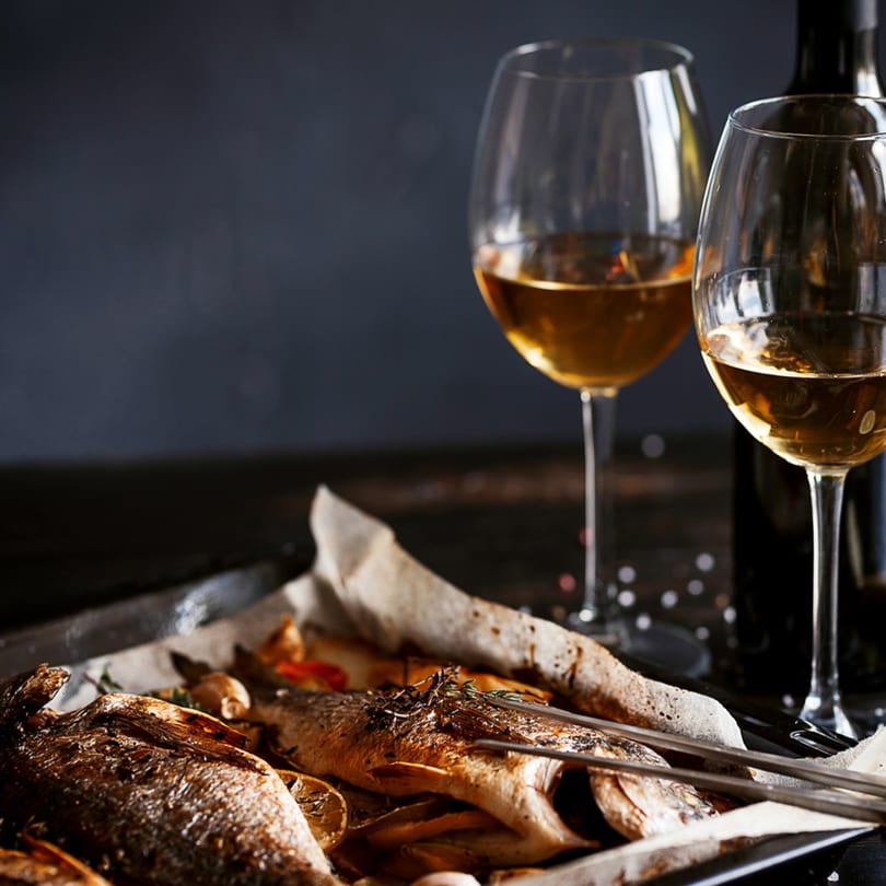 Two whole roasted fish with lemons and herbs, served with two glasses of white wine.