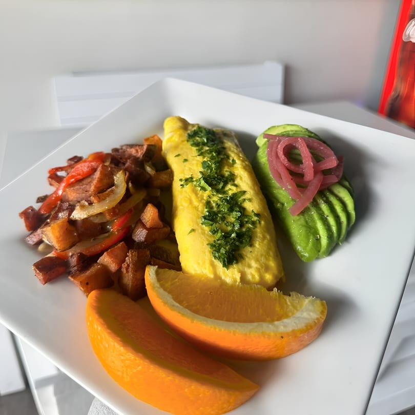 A breakfast plate with an omelet, home fries, sliced avocado with pickled onions, and orange wedges.