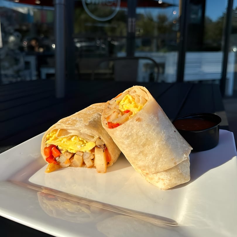 Two breakfast burritos filled with eggs, potatoes, and peppers, served with a side of salsa.
